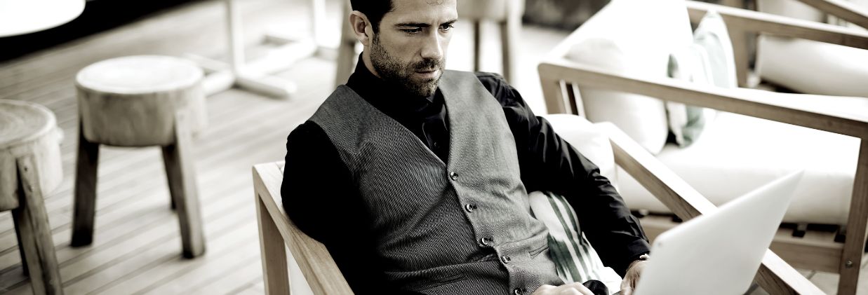 Man in a dark vest using a laptop for divorce mediation while seated on an outdoor wooden chair